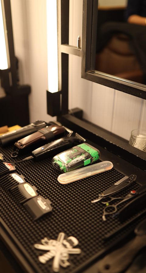 Bancada da Barbearia Constant com máquinas de cortar cabelo, tesouras e navalha arrumadas sobre o tapete preto