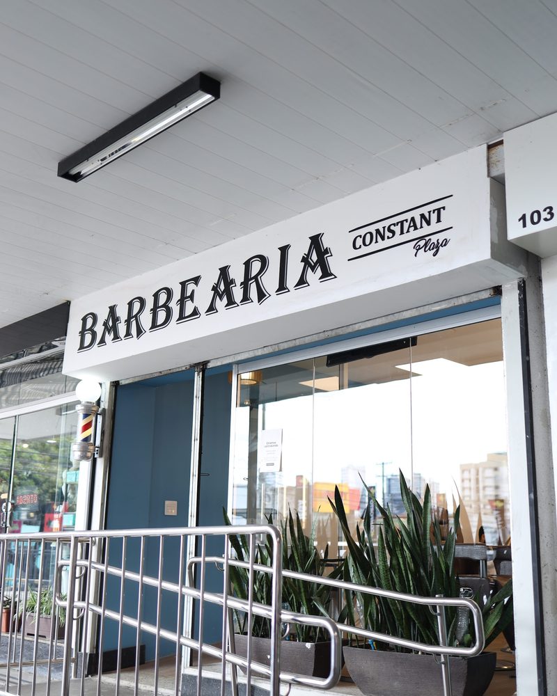 Fachada da Barbearia Constant, com o letreiro BARBEARIA e vasos de plantas na entrada